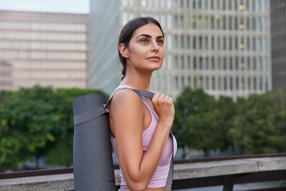 Beautiful woman poses alone on bridge in downtown going to practice flexibility with karemat has regular morning training to keep fit wears sportsclothes does workout wants to stay always healthy